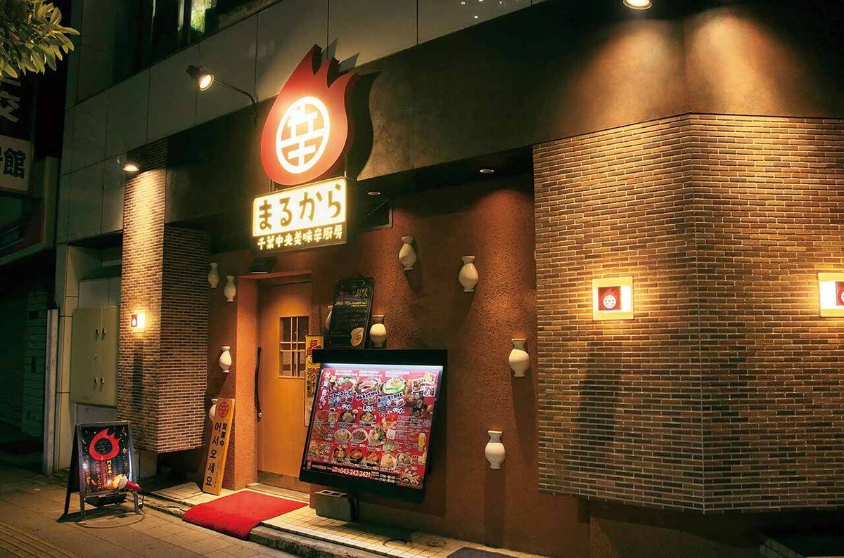 まるから千葉中央店の外観。赤い炎のロゴ看板とレンガの壁
